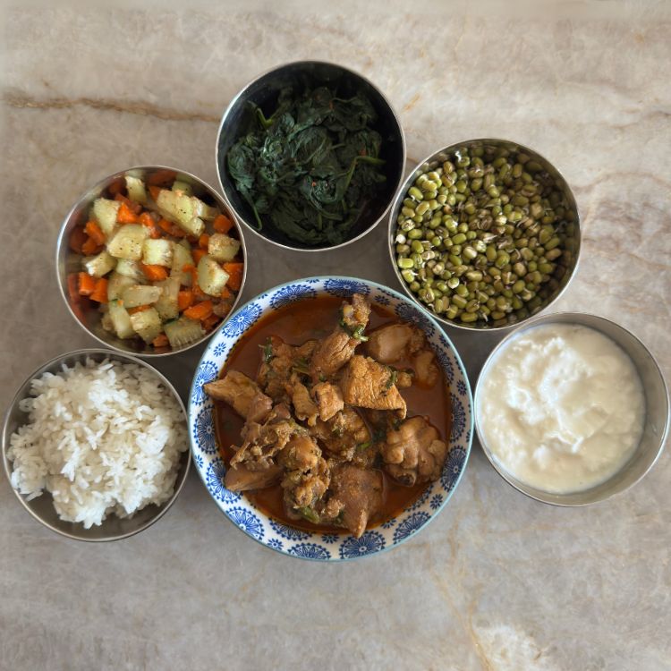 5 side dishes placed around chicken curry for thali experience