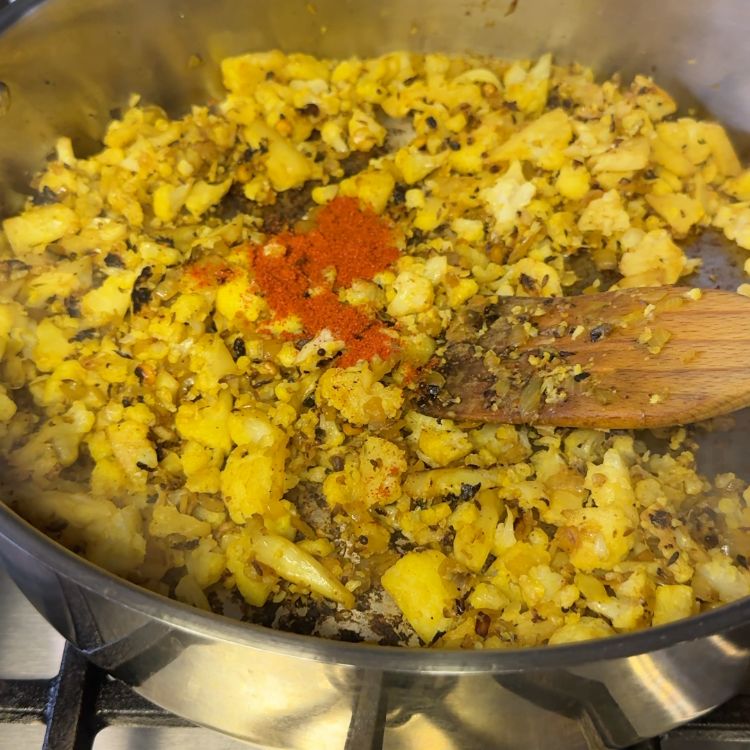 Chili powder being added to the cooking cauliflower for a spicy and flavorful Cauliflower Vepudu Fry.