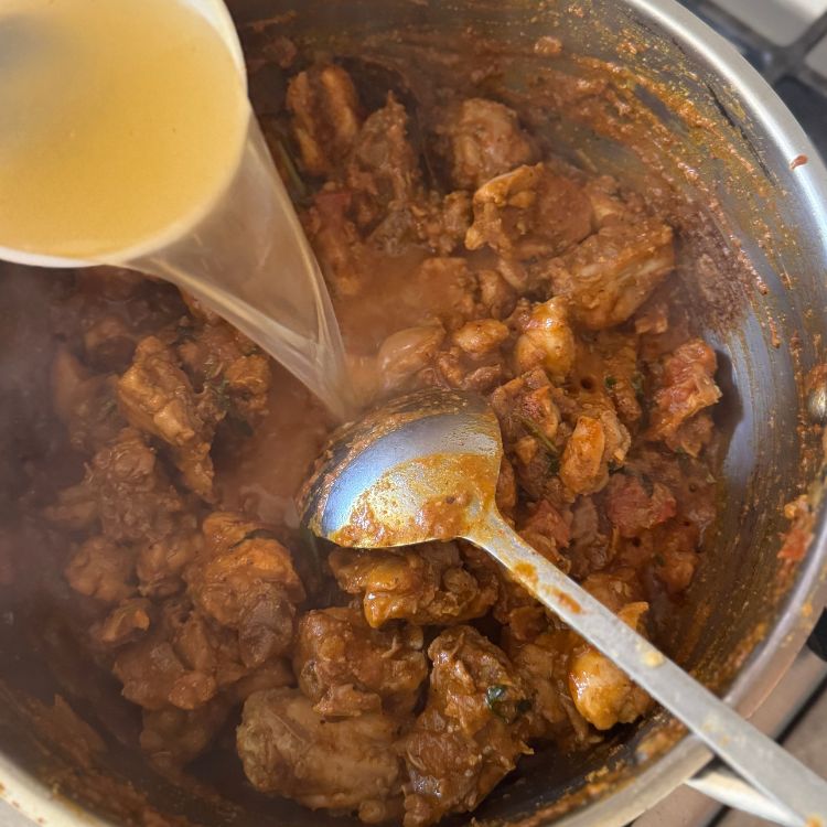 Pouring water on to cooking chicken curry