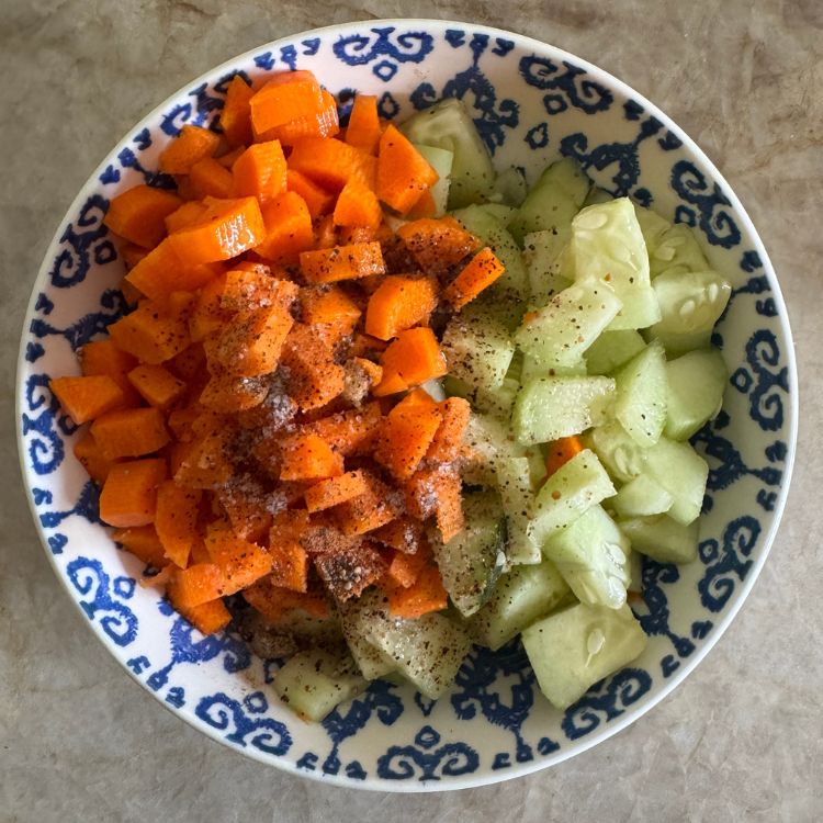 salt and pepper on top of carrot cucumber salad in a bowl