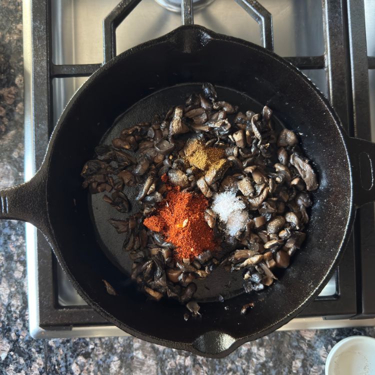 Sprinkling Indian spices like chili garlic powder and cumin over sautéed mushrooms in pan