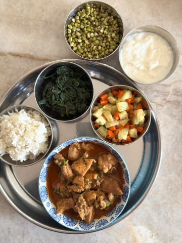 Balanced chicken curry thali with rice, spinach, cucumber carrot salad, and yogurt - nutritionally complete Indian meal