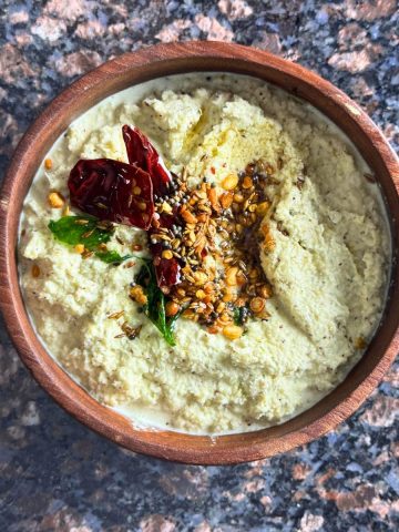 A bowl of creamy coconut chutney garnished with tempered spices, served as a side dish for idlis or dosas.