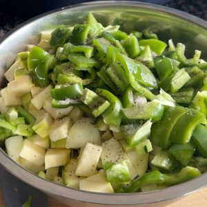 A bowl of zucchini, green peppers, and onions tossed with salt, pepper, and oil before air frying.