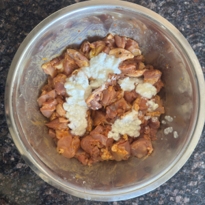 Creamy yogurt being mixed with vibrant Indian spices to create marinade for chicken thighs